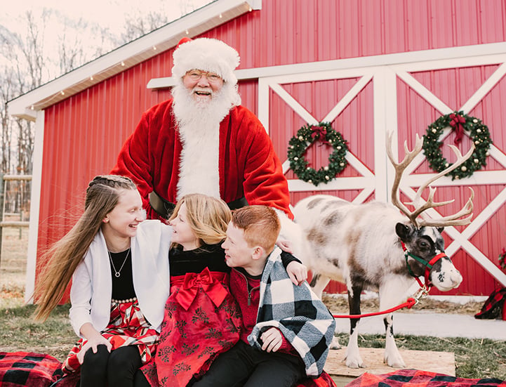 Santa and a live reindeer with children outside the red barn during Christmas at the Farm at Wilderness Valley Farm