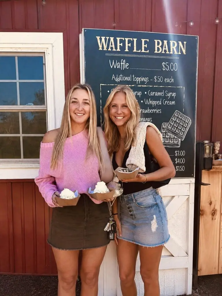 Two young women holding waffles in front of the Waffle Barn menu board at Wilderness Valley Farm near Gaylord, Michigan